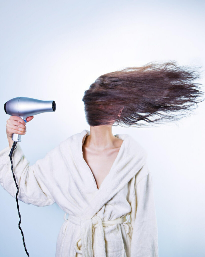 Woman blow-drying her hair with a handheld blow dryer, showcasing essential hair styling tools for everyday beauty routines